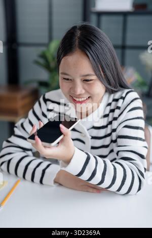 Asian Woman Engaging with Voice Assistant on Smartphone in Modern Home Stock Photo