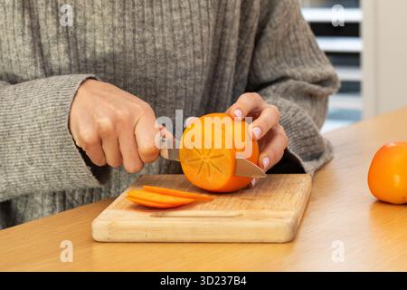 Person slicing fresh persimmon on wooden cutting board Stock Photo
