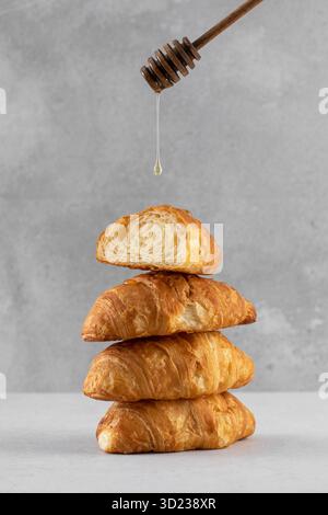 A drop of honey or syrup drips onto a stack of fresh croissants. French breakfast. Stock Photo