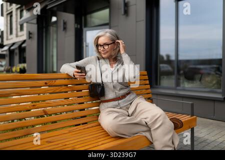 Senior woman sitting on a bench using smartphone in a modern urban area Stock Photo