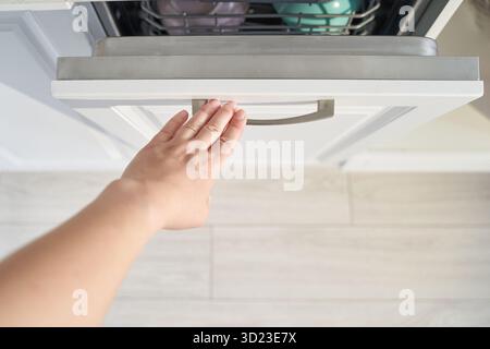 Caucasian female opening kitchen drawer with outstretched hand on white cabinet Stock Photo