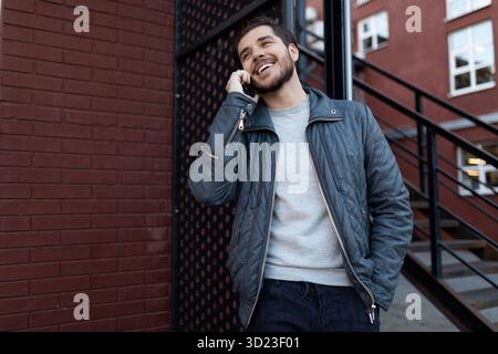 Stylish young caucasian man speaks on a mobile phone against a brick wall Stock Photo