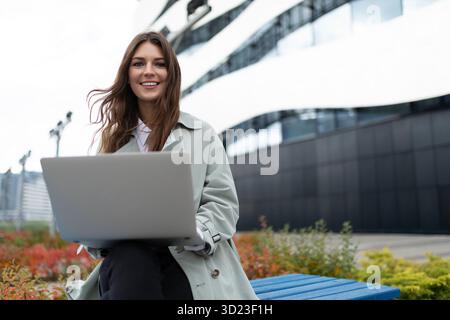 Young woman working on laptop next to office outside Stock Photo