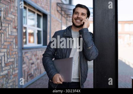 Middle-aged man programmer talking on a mobile phone with a laptop in his hands Stock Photo