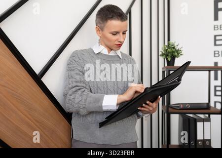 European stylish business woman with a short haircut in the office checking documents in a leather folder Stock Photo