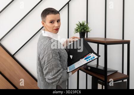 A business woman with a short haircut stands in the office with a folder for documents. Stock Photo