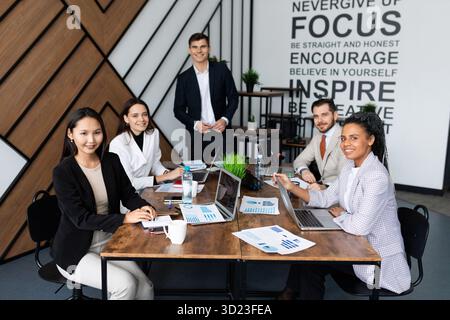 Colleagues in the office at a large working table look at the camera Stock Photo