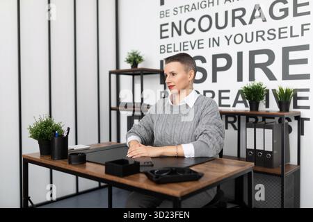 A young businessman in a strict gray suit enjoys listening to music on headphones against the background of an office wall Stock Photo