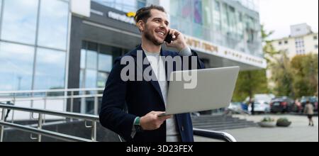 Male Businessman with a laptop in his hands speaks on the phone outside Stock Photo
