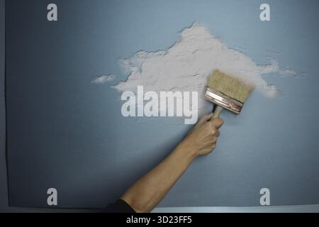 Hand of a person painting a cloud on a sky-blue wall, concept of idea, fantasy, freedom, art Stock Photo