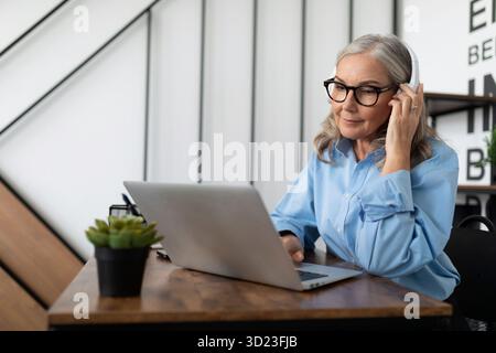 Caucasian businesswoman in headphones watching webinar on laptop in office Stock Photo