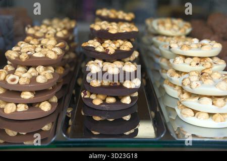 Cookies with hazelnuts covered in milk, dark or white chocolate. Display in bakery shop. Snacks for coffee at showcase in cozy small cafe Stock Photo
