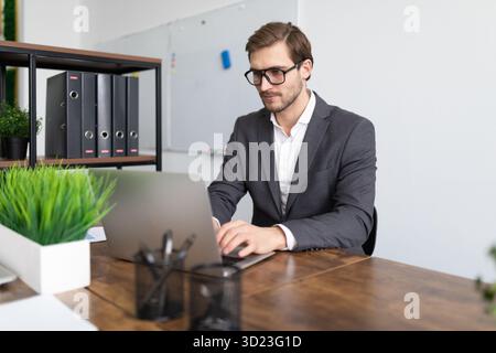 Businessman at a laptop in the office in a formal suit with glasses Stock Photo