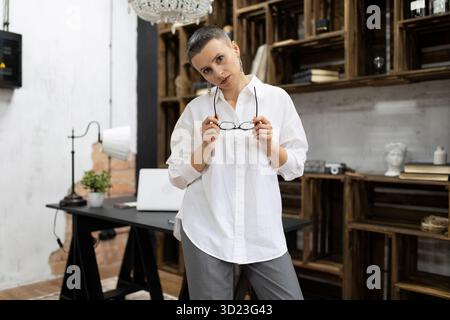 A woman psychologist in the interior of the office carefully looks at the camera with glasses in her hands Stock Photo