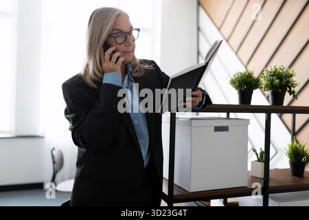 Middle aged older business woman in the office talking on a mobile phone Stock Photo