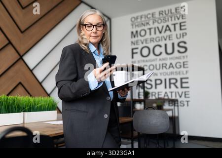 Middle aged older business woman in the office with a phone in her hands Stock Photo