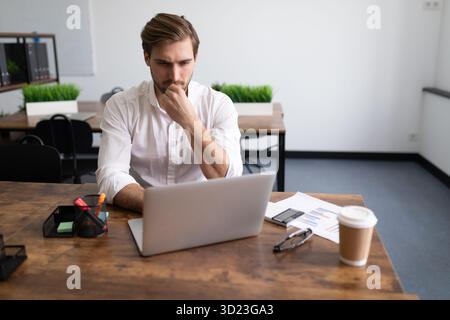 Serious businessman in the office behind a laptop solves a complex business problem Stock Photo