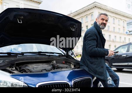 Men sits leaning on a broken car in the city Stock Photo