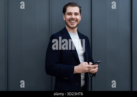 Portrait of a strong middle-aged businessman using a mobile phone and a wide smile against a gray wall Stock Photo