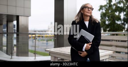 Business woman on the terrace of an office building with a laptop in her hands, caucasian Middle aged older businesswoman at wor Stock Photo