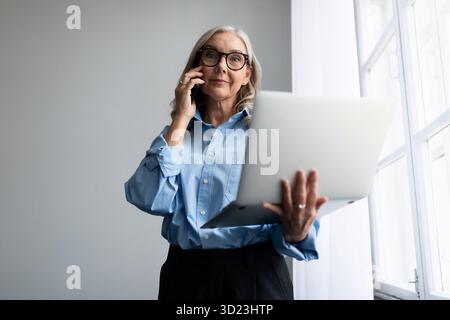 Successful woman manager with a laptop in her hands speaks on a mobile phone at the office window Stock Photo