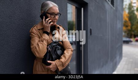 Business senior woman talking on a mobile phone at the entrance to the office Stock Photo