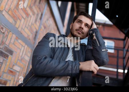 Pensive young man outside looks into the distance on the background of the building Stock Photo