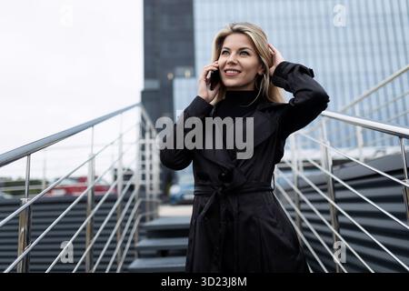 Portrait of a confident middle-aged business woman talking on a mobile phone against the backdrop of an office skyscraper Stock Photo
