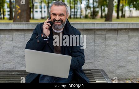 Male businessman working on laptop Park talking on the phone smiling looking at camera Stock Photo