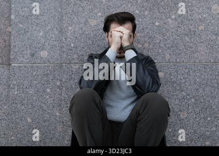 Grieving man sitting upset covering his face with his hands Stock Photo