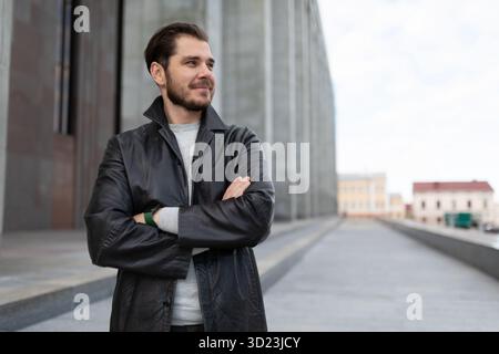 Pretty young caucasian man with hands on his chest stands against the background of a gray building Stock Photo