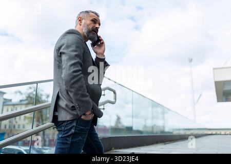 Portrait of a mature business man talking on a mobile phone on the stairs at the entrance to the office Stock Photo
