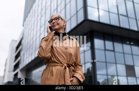 Successful elderly stylish businesswoman outside office building talking on the phone Stock Photo