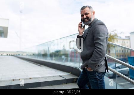 Mature adult businessman talking on the phone turning around looking smiling at the camera Stock Photo