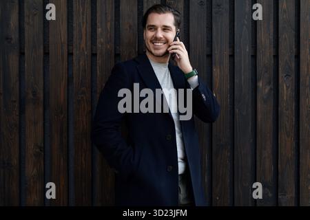 Portrait of a male businessman in business clothes talking on the phone against a wooden dark wall Stock Photo