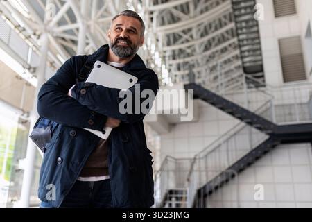 Portrait of a successful adult Gray-haired businessman with a laptop in his hands on the background of the airport Waiting room, Stock Photo