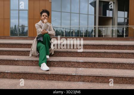Serious african american woman lawyer sitting on steps of city building Stock Photo