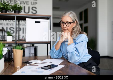 Adult mature business woman sitting at the office desk at work looking at documents. Accounting Bookkeeper Clerk Woman concept Stock Photo