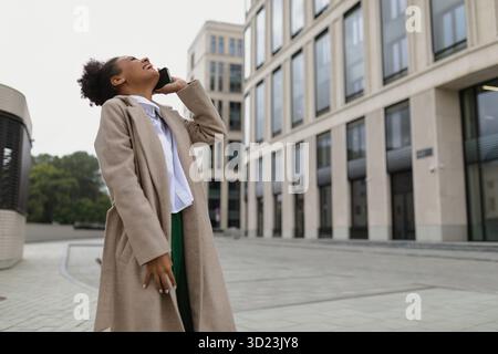 Young african american woman talking on mobile phone outside with her head thrown back and laughing Stock Photo