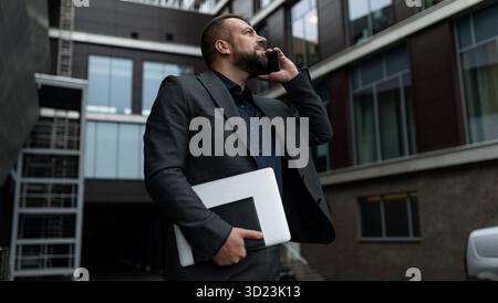 Business man talking on a mobile phone with a laptop in his hands on the background of a business center, mobile internet bankin Stock Photo