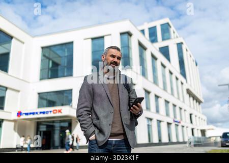 Adult business businessman 50 years old against the background of a business center with a mobile phone in his hands Stock Photo