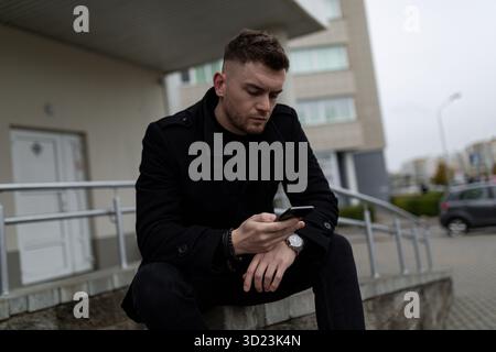 Young man sitting and looking at mobile phone outside Stock Photo