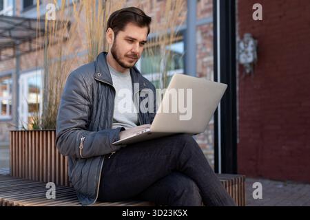 Young man working on a laptop on the street next to a brick building Stock Photo