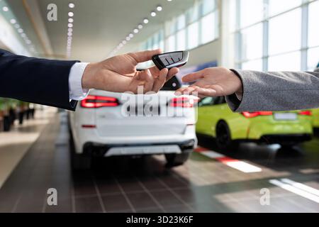 Handing over the keys close-up by the seller of the car dealership to the buyer on the background of new cars Stock Photo