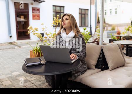 Adult businesswoman working on a laptop at a table in a city cafe Stock Photo