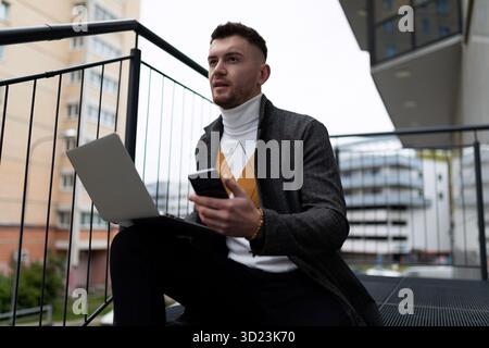 Young male businessman makes a purchase online using smartphone and laptop Stock Photo