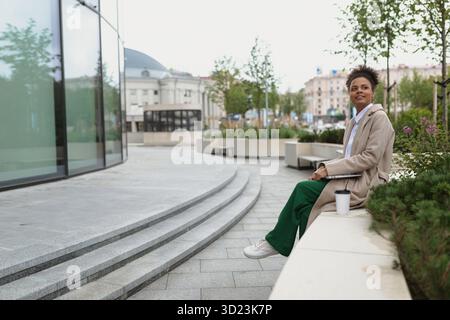 Business african american young woman working with laptop while sitting next to her own building Stock Photo
