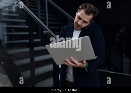 Young business man talking on the phone with a laptop in his hands outside the office Stock Photo