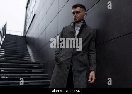 Elegant caucasian middle aged man in coat leaning against wall outside Stock Photo