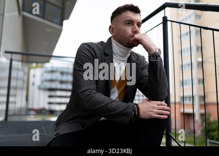Portrait of a thoughtful young man sitting on the steps next to his own building Stock Photo